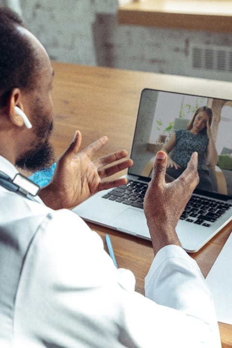 Doctor advising the patient online with laptop. African-american doctor during his work with patients, explaining recipes for drug. Daily hard work for health and lives saving during epidemic.